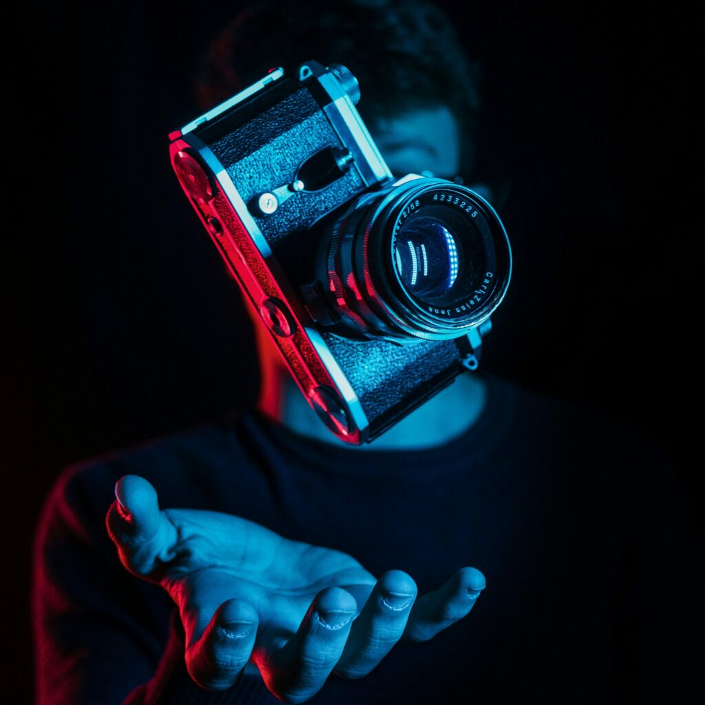 Appareil photo vintage flottant au-dessus de la main d’un homme, éclairé par une lumière bleue et rouge dans une ambiance sombre et artistique