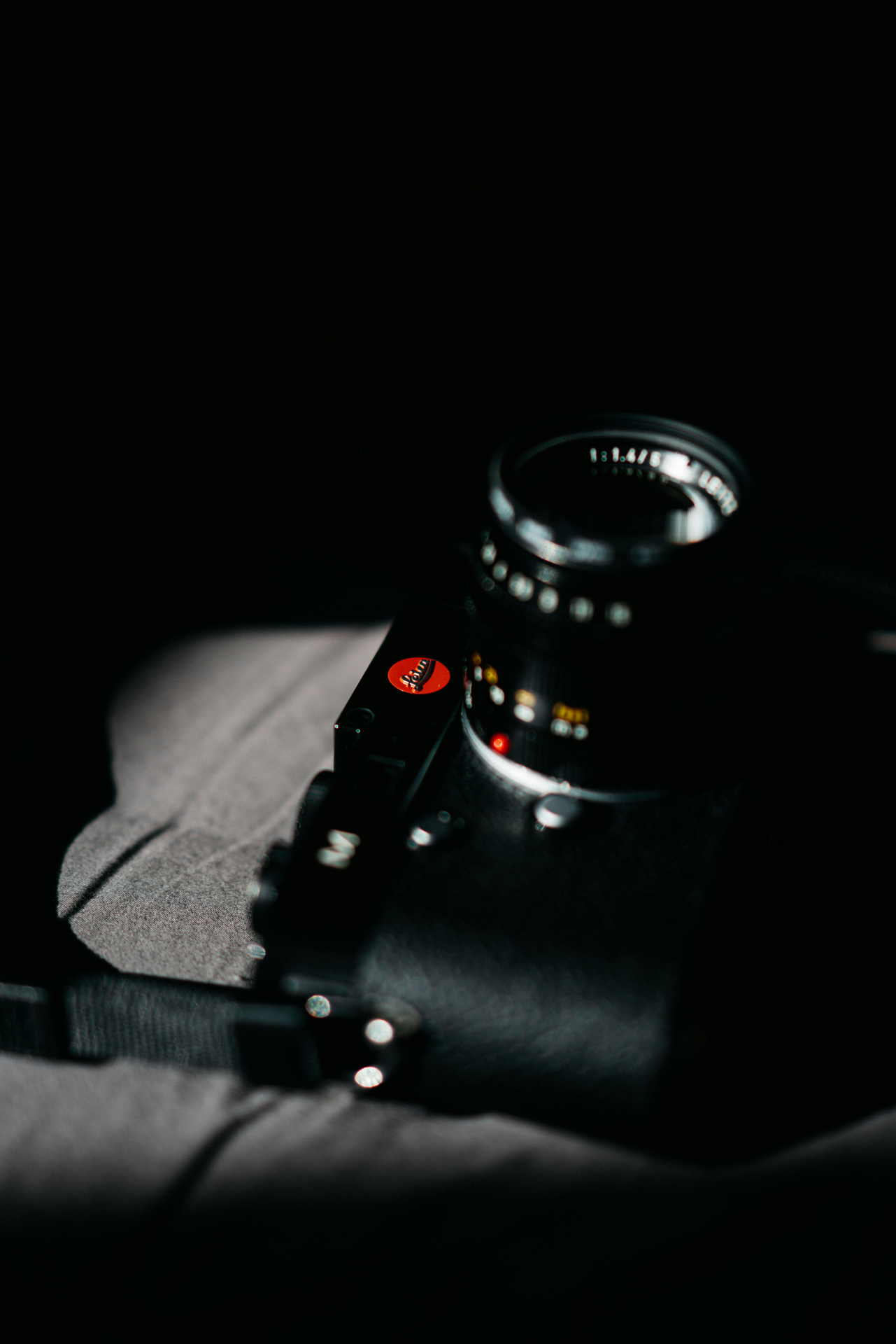 Appareil photo Leica posé sur un tissu sombre, avec une lumière dirigée mettant en valeur le logo rouge emblématique et l’objectif partiellement dans l’ombre